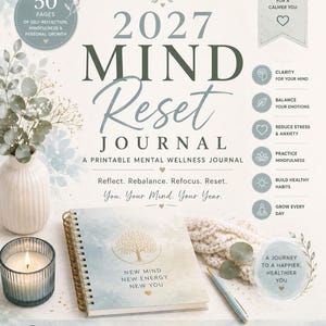 Op de afbeelding: Een 2027 Mind Reset Journal met spiraalbinding, voorzien van een gouden boomillustratie en de tekst New Mind New Energy New You. De kaft heeft een zacht blauw en wit aquarelontwerp. Het wordt gepresenteerd met een kaars en een pen.