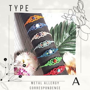 Può includere: Una pila di sei braccialetti colorati con pietre di diversi colori. I braccialetti sono realizzati con una tecnica di annodatura macramé. Il testo "TYPE" e "METAL ALLERGY CORRESPONDENCE A" è visibile nell'immagine.