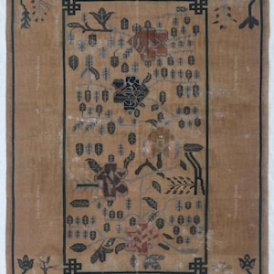 May include: A rectangular area rug featuring a tan background with a dark brown border. The design includes stylized floral motifs and leaf patterns in shades of brown, gray, and muted orange, arranged within a central rectangular frame.