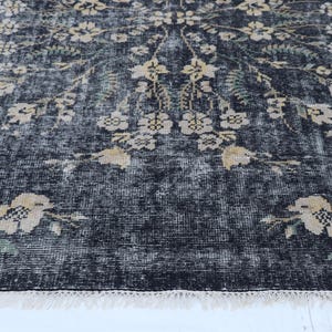 May include: A distressed black rug with a floral pattern in cream and green. The rug has a faded, vintage look with a fringed edge. The floral design is spread across the rug.