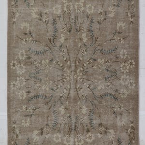 May include: Rectangular beige rug with a floral pattern. The rug features a central floral design with surrounding floral borders. The flowers are in shades of white, beige, and blue. The rug has a fringed edge.