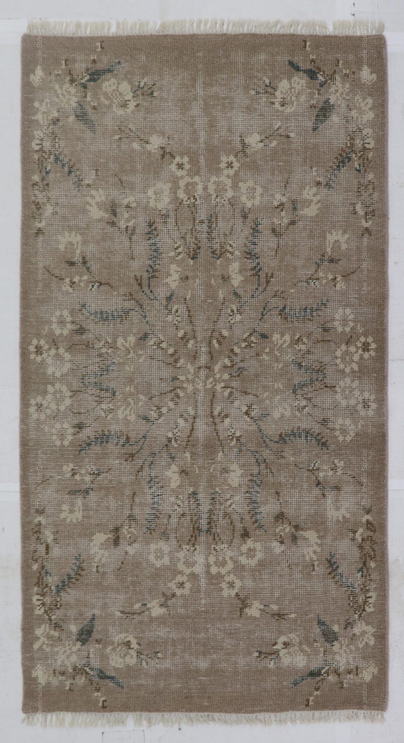May include: Rectangular beige rug with a floral pattern. The rug features a central floral design with surrounding floral borders. The flowers are in shades of white, beige, and blue. The rug has a fringed edge.