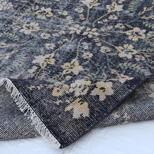 May include: A dark blue rug with a floral pattern in cream and green. The rug has a distressed look, with a fringe along the edge. The floral design is spread across the rug's surface.