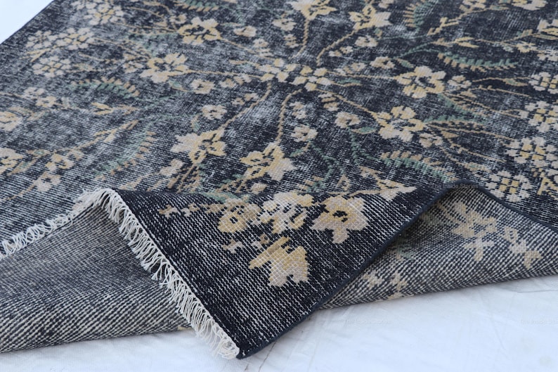 May include: A dark blue rug with a floral pattern in cream and green. The rug has a distressed look, with a fringe along the edge. The floral design is spread across the rug's surface.