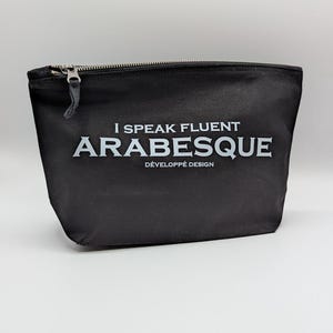 Könnte beinhalten: Schwarze Reißverschlusstasche mit dem Text "I Speak Fluent Arabesque" in Weiß. Die Tasche hat einen silbernen Reißverschluss und einen kleinen Leder-Zuglasche. Darunter steht "Développé Design".