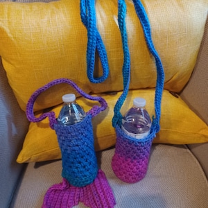 May include: Two handmade crochet water bottle holders. One is blue and purple with a mermaid tail design. The other is a simple cylinder shape in shades of purple and blue. Both have a strap for carrying.