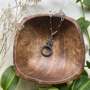 以下が含まれることがあります： 円の中に十字架が入った円形の銀製のペンダントが付いた銀色のチェーンネックレス。ネックレスは木製のボウルに入っています。