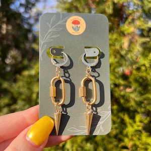 May include: Gold and silver clip-on earrings with a chain and a gold oval link. The earrings have a gold spike charm.