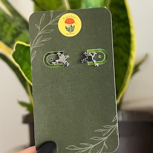 May include: A pair of silver frog stud earrings on a green card with the text "Earth Star" and a mushroom illustration.