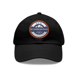 Könnte beinhalten: Schwarze Baseballkappe mit einem kreisförmigen Aufnäher mit einer Bergkette und dem Text "PNW WASHINGTON LEAVENWORTH 1997". Der Aufnäher hat ein blaues und orangefarbenes Farbschema.