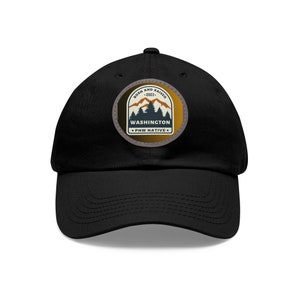 May include: Black baseball cap with a circular patch featuring a mountain scene and the text "BORN AND RAISED - 2003 - WASHINGTON - PNW NATIVE." The patch has brown, tan, and blue colors. The cap is made of a soft material and has a curved brim.