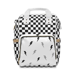 May include: A black and white checkered backpack with a white front pocket featuring a lightning bolt pattern. The backpack has a white handle and straps, and gold-colored zippers. The bag has side pockets and a top handle.