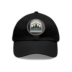 May include: Black baseball cap with a circular patch featuring a mountain and tree design. The patch reads "BORN AND RAISED - 2001 - LEAVENWORTH - NORTH CENTRAL WA". The cap has a curved brim and a structured crown.