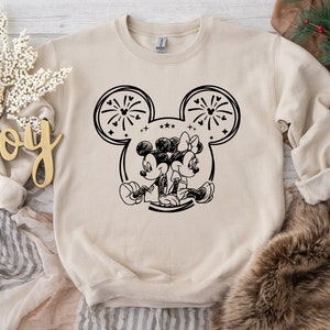 May include: Beige sweatshirt featuring a black and white illustration of Mickey and Minnie Mouse. The design includes fireworks and stars within the iconic mouse ears. The sweatshirt is a crew neck style.