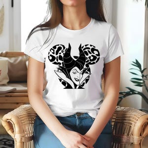 May include: White t-shirt with a black and white graphic of a Disney villain. The design features the character's face and horns within a Mickey Mouse silhouette, with leopard print ears. The shirt has a classic crew neck.