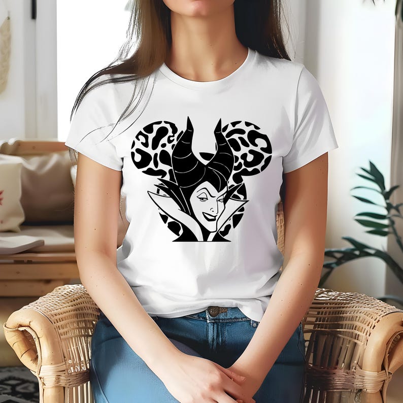 May include: White t-shirt with a black and white graphic of a Disney villain. The design features the character's face and horns within a Mickey Mouse silhouette, with leopard print ears. The shirt has a classic crew neck.