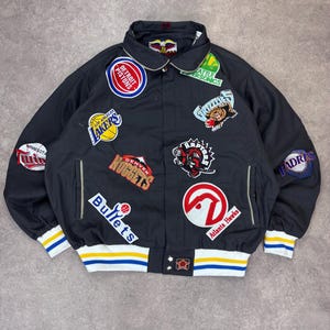 Könnte beinhalten: Schwarze Satin-Bomberjacke mit mehreren Teamlogo-Patches, darunter die Lakers, Pistons und Nuggets. Die Jacke hat eine Knopfleiste, Seitentaschen und gestreifte Bündchen und Saum in Weiß, Gelb und Blau.