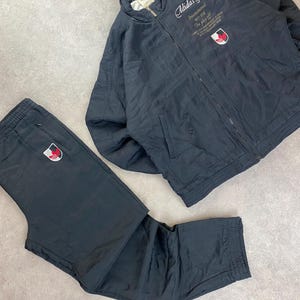 May include: Black Adidas track suit set. The set includes a zip-up jacket with "Adidas Sports" text and a logo patch, and matching track pants. The jacket and pants have a sporty, casual style, suitable for athletic wear or everyday use.