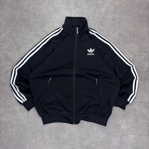Könnte beinhalten: Schwarze Trainingsjacke mit weißen Streifen auf den Ärmeln und einem weißen Logo auf der Brust. Die Jacke hat einen durchgehenden Reißverschluss, zwei Vordertaschen sowie einen gerippten Kragen und Bündchen. Hergestellt aus glattem, sportlichem Material.