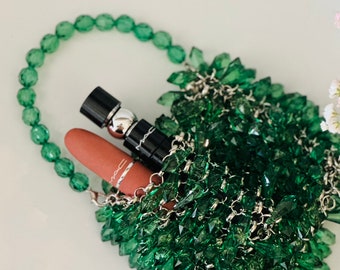Puede incluir: Un pequeño bolso de cuentas verdes con una cadena plateada y un lápiz labial y una botella de suero en su interior.