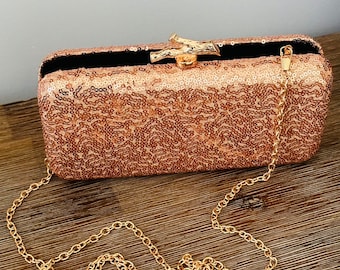 May include: A rose gold sequined clutch with a gold chain strap and a gold, tree-branch-shaped clasp.