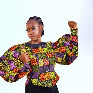 May include: A woman wearing a black and yellow patterned blouse with puffed sleeves. The blouse has a geometric design with red, purple, and orange accents.