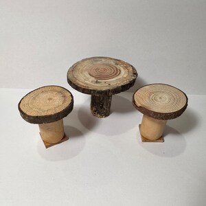 May include: Three wooden tables made from tree slices. The largest table is round and has a natural wood finish. The two smaller tables are round and have a natural wood finish. The tables are all on a white background.