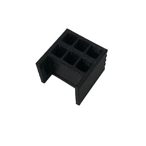 Op de afbeelding: Een zwart plastic 3D-geprint object met een rasterpatroon en een rechthoekige opening. Het object is ontworpen om te worden gebruikt als een standaard of ondersteuning.