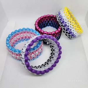 May include: Four colorful beaded bracelets, each with a different color scheme. The bracelets are made with small, round beads in a chainmail pattern. The colors include blue, pink, white, yellow, black, and purple.
