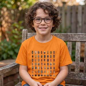 Peut inclure: Un t-shirt orange vif à manches courtes avec un motif en grille composé de diverses petites illustrations d'insectes imprimées sur le devant. Le graphique présente plusieurs rangées et colonnes de différents insectes aux couleurs variées.