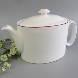May include: White ceramic teapot with a red rim and a lid. The teapot has a handle and a spout.