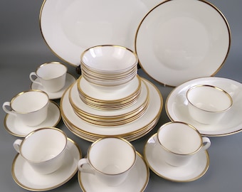 Op de afbeelding: Een set wit porselein serviesgoed met gouden rand. De set bevat borden, kommen en kopjes.