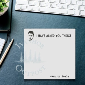 May include: A white notepad with a black border and the text "I HAVE ASKED YOU THRICE" printed on it. The notepad also features a black and white illustration of a man's face and a logo with the text "IVANHOE OUTPOST" in a blue and white color scheme. The text "*Not to Scale" is printed at the bottom of the notepad.