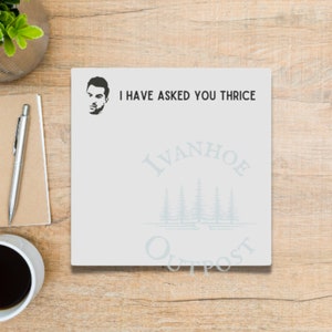 May include: White notepad with a black and white illustration of a man's face and the text "I have asked you thrice". Below the text is a logo with the text "Ivanhoe Outpost" in a light blue color.