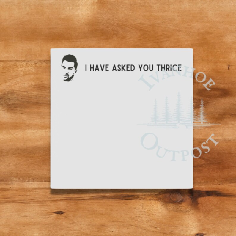 May include: A white notepad with the text "I have asked you thrice" printed on it. The notepad has a black and white illustration of a man's face in the top left corner. The notepad is on a wooden surface.