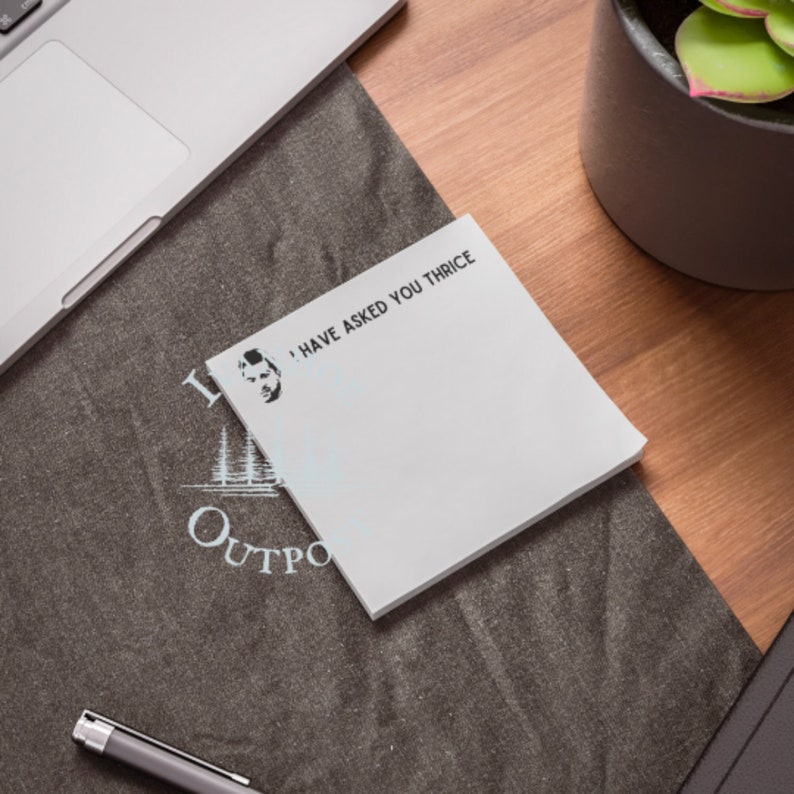 May include: White sticky note with the text "I have asked you thrice" and a black and white illustration of a man's face. The note is on a dark gray surface with a blue and white logo that says "Outpost".