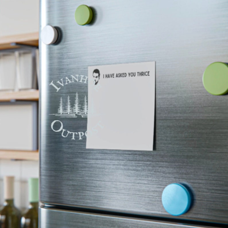 May include: A white refrigerator with a white sticker that says "I have asked you thrice" and a black and white logo that says "Ivanhoe Outpost". There are three green and one blue round magnets on the refrigerator.