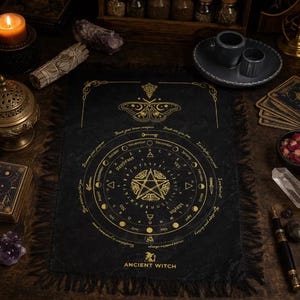 Puede incluir: Un paño de altar rectangular negro con diseños impresos en oro, que incluyen un pentagrama central, el alfabeto, los meses y un motivo de polilla. La tela tiene bordes con flecos y el texto ANCIENT WITCH en la parte inferior, rodeado de objetos ocultos.