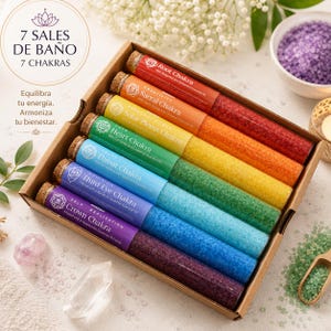 Puede incluir: Una caja de cartón con siete tubos de ensayo de vidrio llenos de sales de baño de colores, cada uno etiquetado con un nombre de chakra: Raíz, Sacro, Plexo Solar, Corazón, Garganta, Tercer Ojo y Corona. Las sales corresponden a los colores rojo, naranja, amarillo, verde, azul, índigo y violeta.