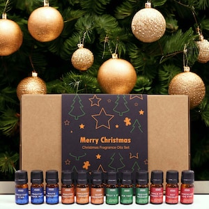 Può includere: Una scatola rettangolare in cartone etichettata Merry Christmas Christmas Fragrance Oils Set con una fascia nera che presenta disegni al tratto verdi e arancioni di stelle, alberi e omini di pan di zenzero, con undici boccette di olio.