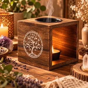 Peut inclure: Un brûle-parfum carré en bois brun foncé avec une gravure d'arbre de vie dans un cercle sur la face avant. L'objet possède une coupelle en métal noir sur le dessus pour l'huile et un espace intérieur creux contenant une bougie chauffe-plat allumée.