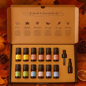 Puede incluir: Una caja de cartón que contiene doce frascos pequeños de vidrio ámbar con tapas negras, dispuestos en dos filas. La tapa interior presenta el texto A Guide to Essential oils y enumera seis categorías: Focus, Uplift, Meditate, Energy, Enliven y Healing.