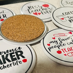 May include: A set of ten white round coasters with black text and red apple graphics. The coasters feature different teacher-themed sayings, including "Living that Teacher Life", "Best Teacher Ever", "Coffee Teach Repeat", "Difference Maker #teacherlife", and "My Favorite People Call Me Teacher".