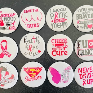 Può includere: Dodici bottoni rotondi bianchi con disegni di nastro rosa e vari messaggi relativi alla consapevolezza del cancro. I messaggi includono "Save the Tatas", "Indossare il rosa per la mia mamma", "Non ho mai saputo cosa fosse il coraggio fino a quando non l'ho visto in mia mamma", "Speranza", "Fede speranza cura", "Tifare per la cura", "FU Cancer", "F*ck Cancer", "Sopravvissuto", "Sostieni i combattenti ammira i sopravvissuti onora i caduti", e "Non arrenderti mai!"