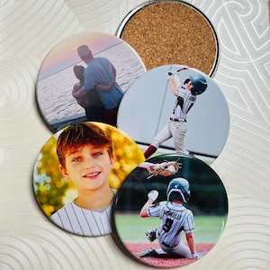 Puede incluir: Un conjunto de posavasos redondos con fotografías. Un posavasos muestra a un niño sonriendo, otro a un jugador de béisbol bateando y un tercero a un jugador de béisbol deslizándose hacia la base. Los posavasos restantes muestran a una pareja abrazándose y un reverso de corcho.