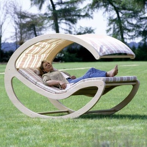 May include: A wooden rocking chair with a canopy and a patterned fabric cushion. The chair is on a grassy lawn.