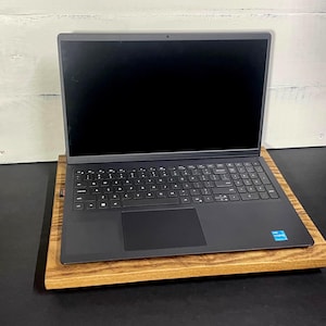 May include: A black laptop computer with a blank screen sits on a stained wooden laptop stand. The stand is rectangular and has a natural wood grain finish. The laptop has a full keyboard and a touchpad.