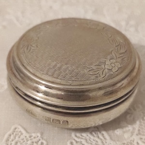 May include: A silver round trinket box with an engraved floral design and the date 1900 on the bottom.