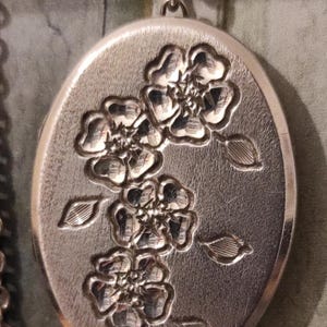 May include: Silver locket necklace with a floral design. The locket is oval shaped and features a delicate chain.