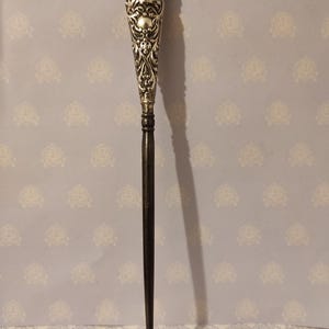 Puede incluir: Un calzador de plata con un diseño floral ornamentado en el mango. El mango es de plata y el eje es negro.